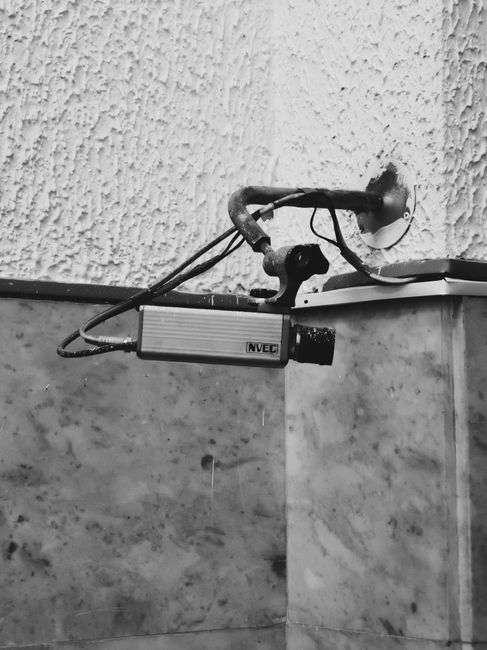 Monochrome image of an indoor CCTV camera mounted on a textured wall.