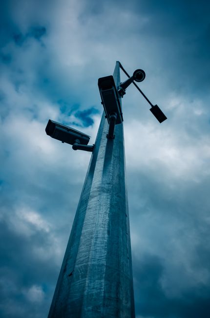Low-angle shot of CCTV cameras mounted on a tall pole against a cloudy sky.